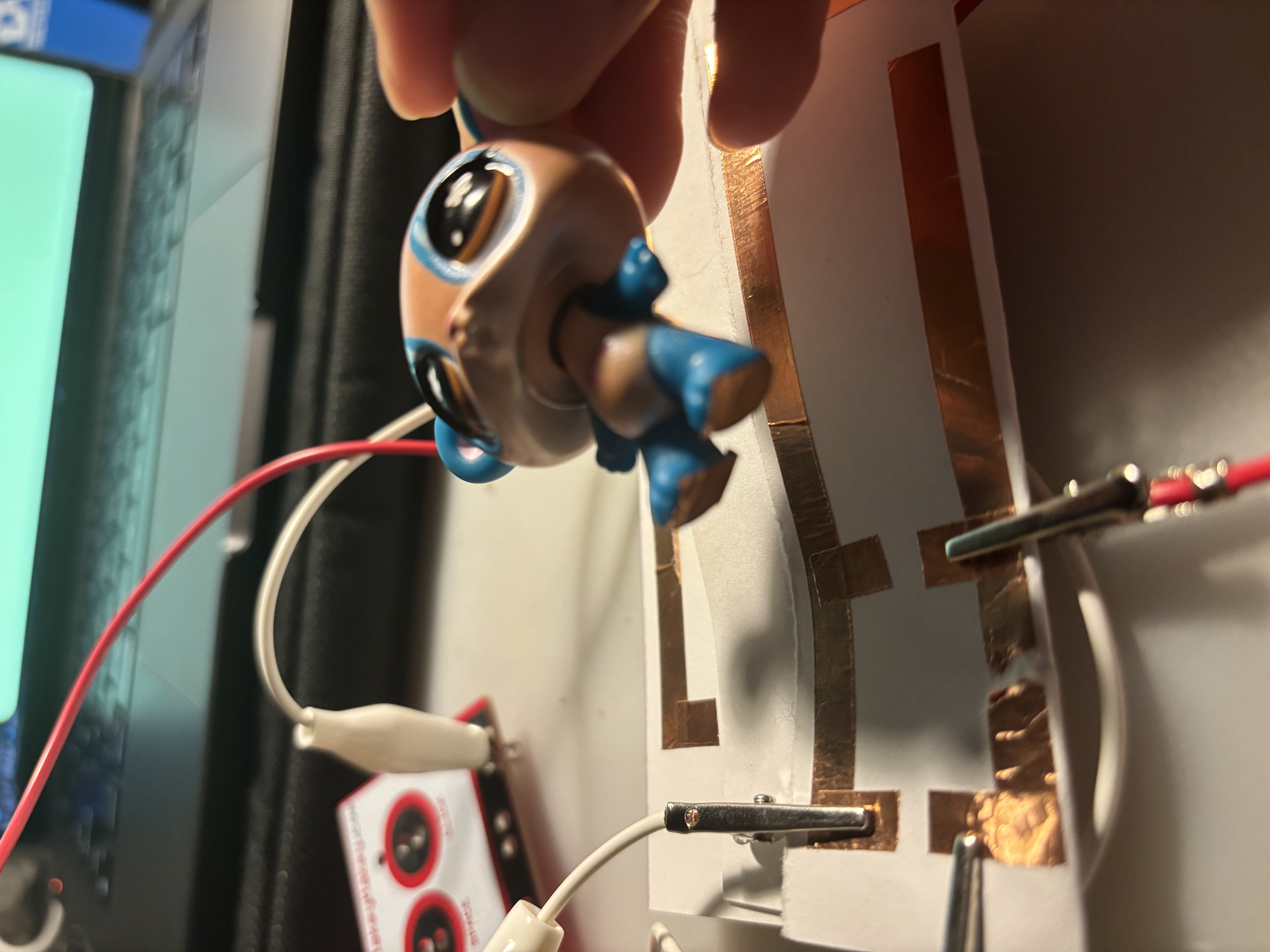 Attaching copper tape to the bottom of a toy character to make it responsive to the old circuit attached to the Makey Makey.